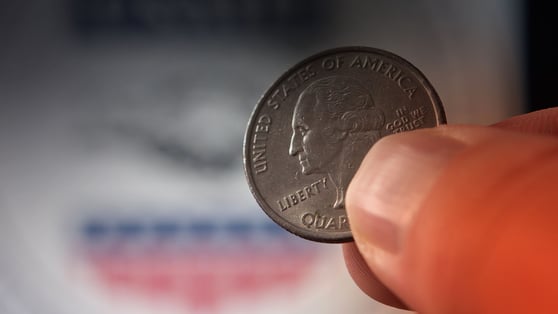 US Quarter Dollar Coin Held in Fingers Against USAID Logo Background