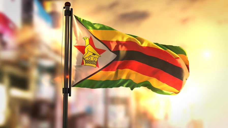 Zimbabwe Flag Against City Blurred Background At Sunrise Backlight