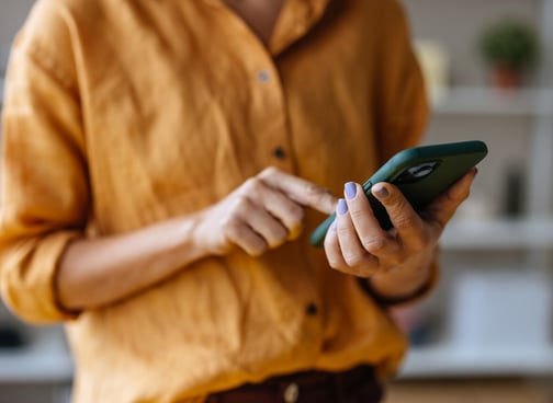 A close up view of a woman texting on her smartphone while standing indoors